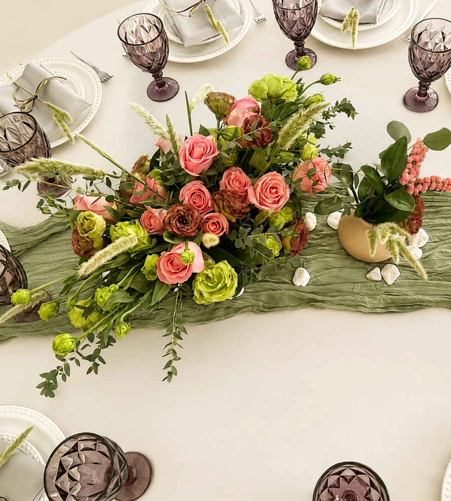 Centro de mesa elegante con rosas en tonos rosa y verdes sobre camino de mesa verde