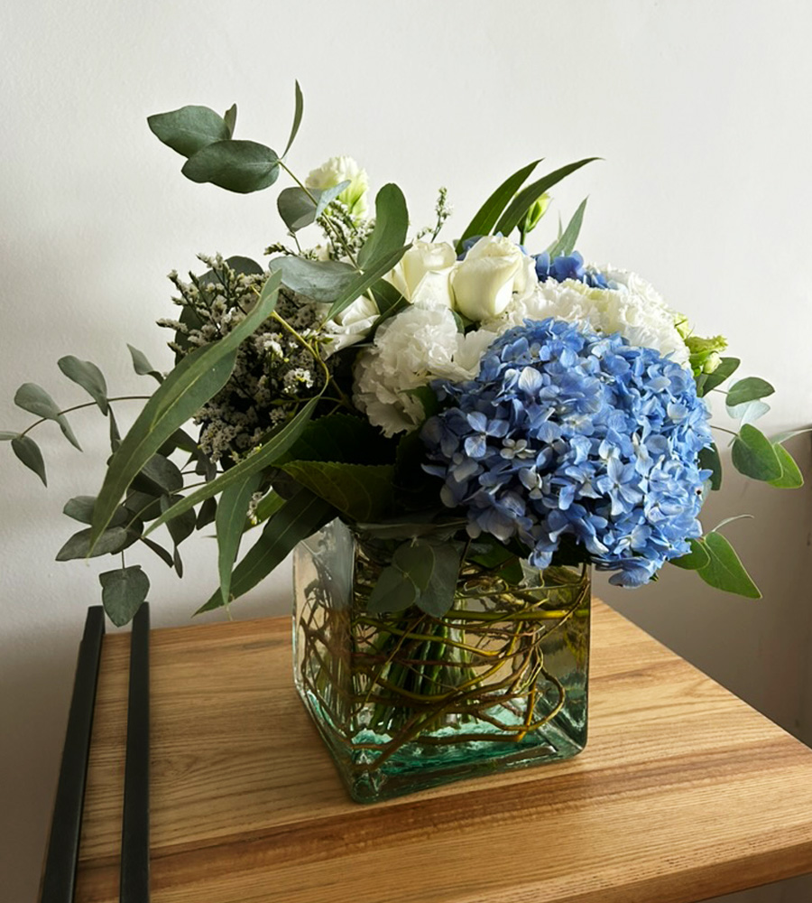 Arreglo floral con hortensias azules y flores blancas en base de vidrio