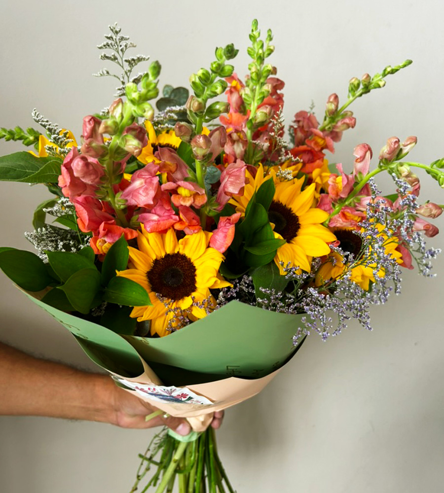 Bouquet con girasoles y flores en tonos coral envuelto en papel