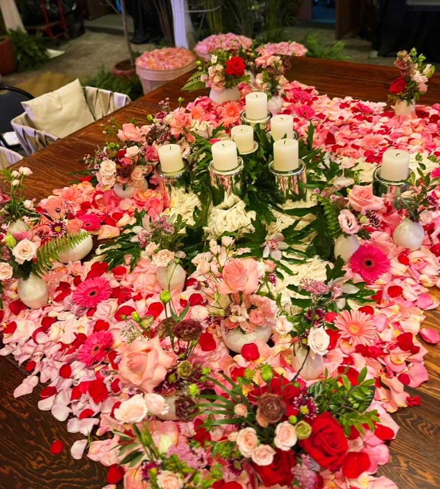 Mesa decorada con pétalos, velas y arreglos florales para evento