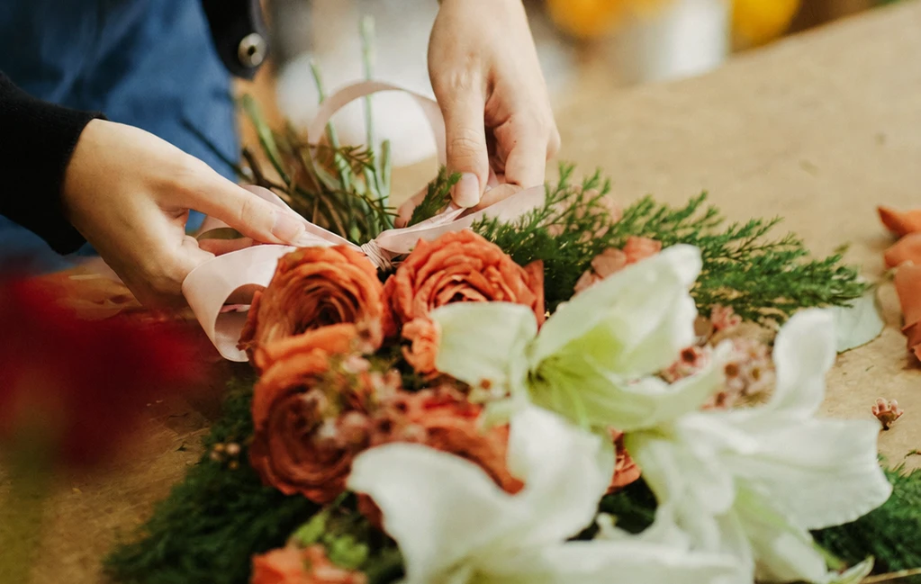 Manos atando un bouquet con listón sobre mesa de trabajo