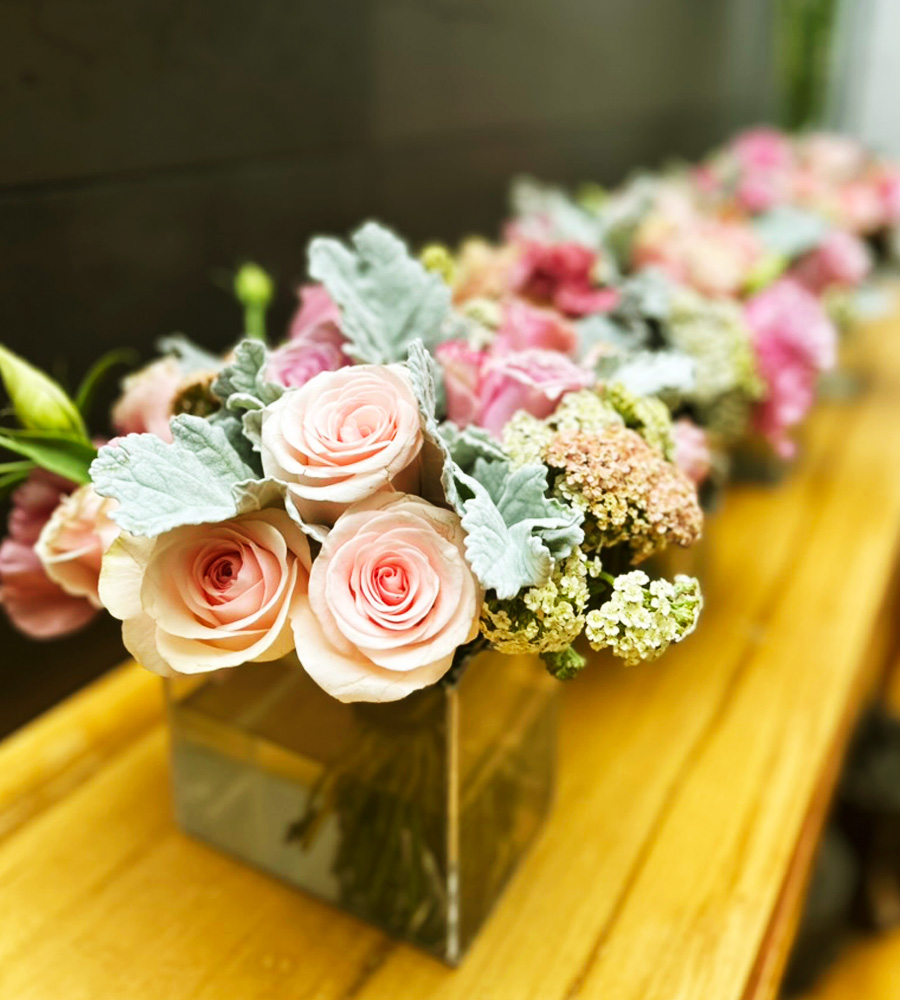 Línea de arreglos florales con rosas rosadas sobre mesa de madera
