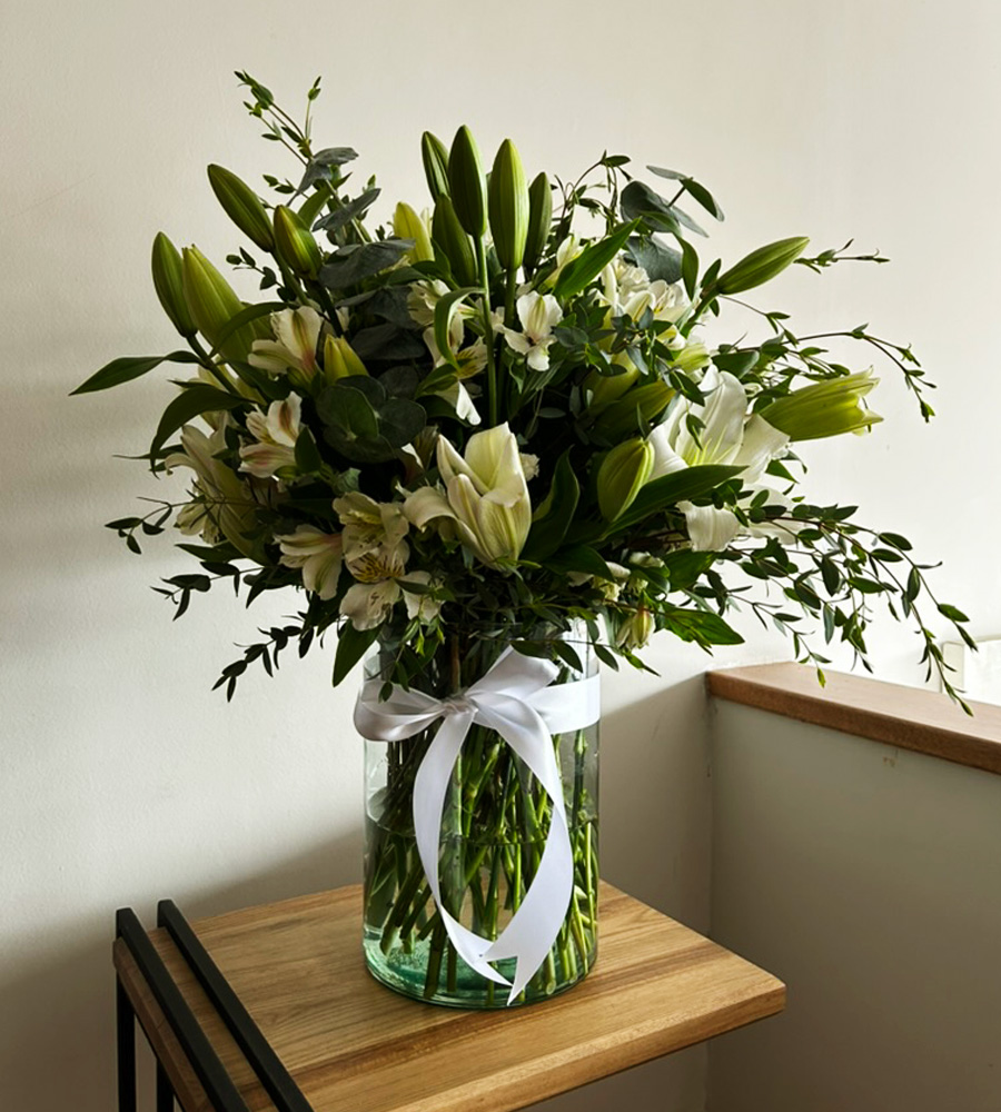 Arreglo floral blanco con lilis y follaje verde en florero de vidrio